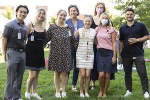 A group of staff members stand on a grassy lawn and smile for the camera.
