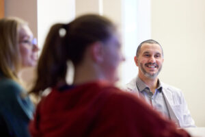 Amjad Musleh, MD, smiles and looks forward as he talks with two students, whose side profiles are blurred out in the foreground. Matt Miller/WashU Medicine