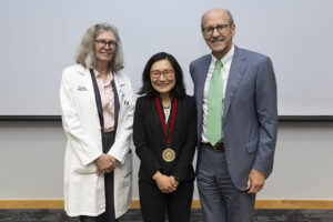 Three physicians pose for photo. Person in the middle is wearing a medal.
