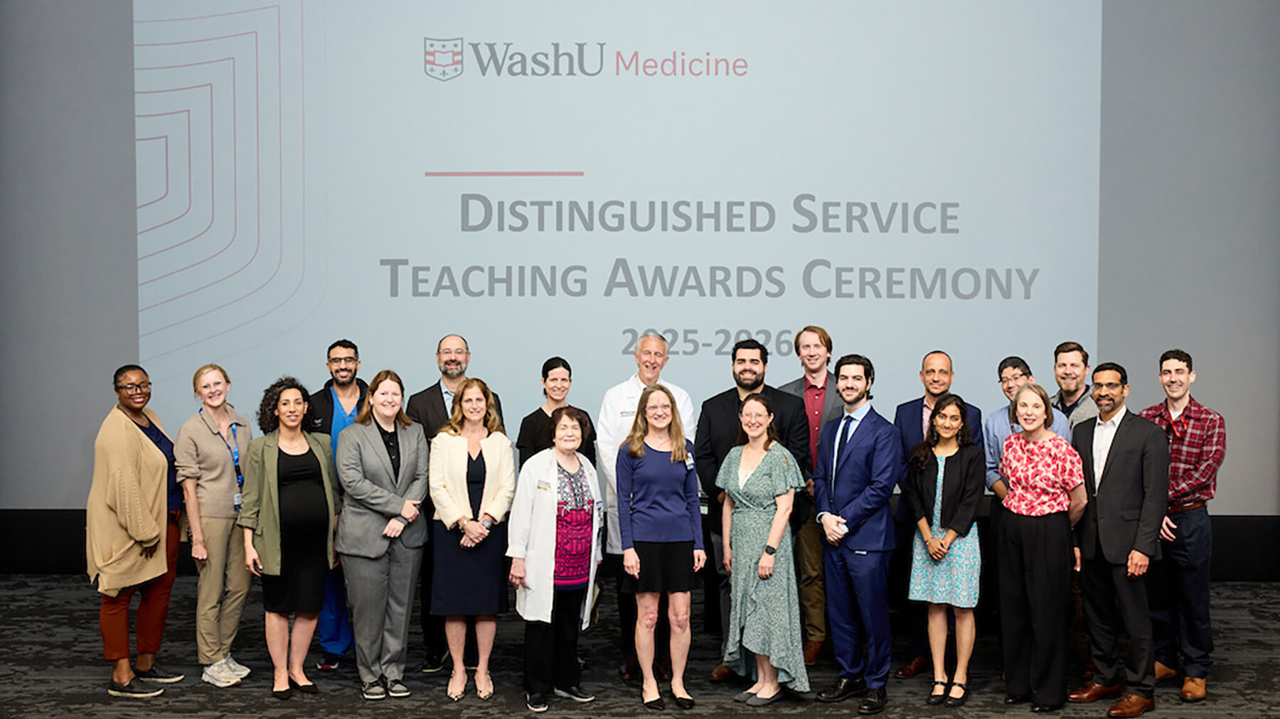 More than 20 people stand on stage, posing for photo