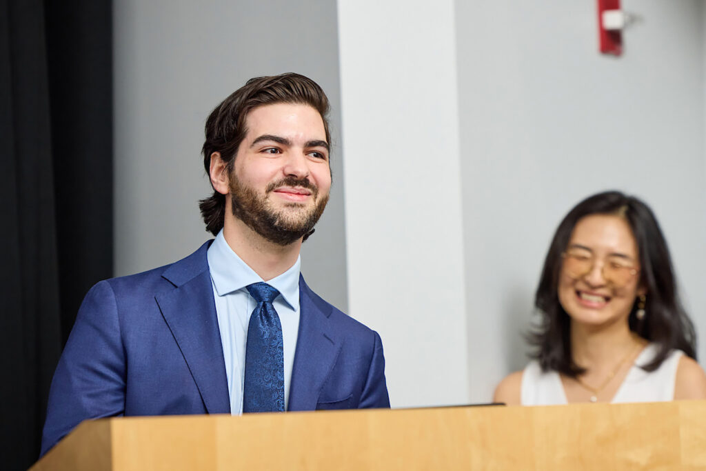 Man in blue suit stands at podium, smiling