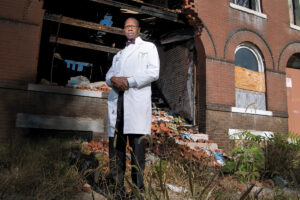 Image of man in white coat standing in rubble of a building