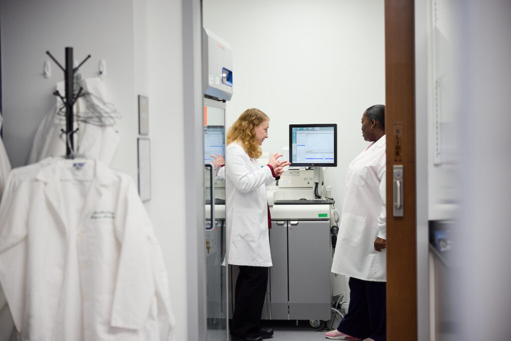 Researchers in white coats are shown conversing through a doorway.