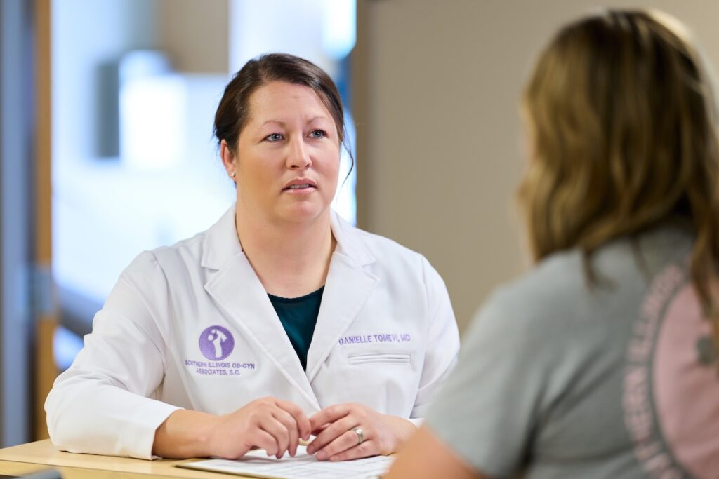 A healthcare professional in a white coat talks with staff