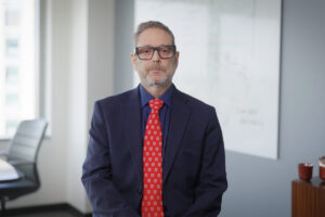 Man wearing glasses and blue suit with red tie, sitting