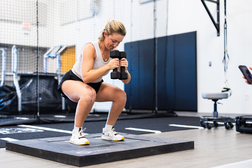 Woman holding dumbbell weights is squatting on a platform